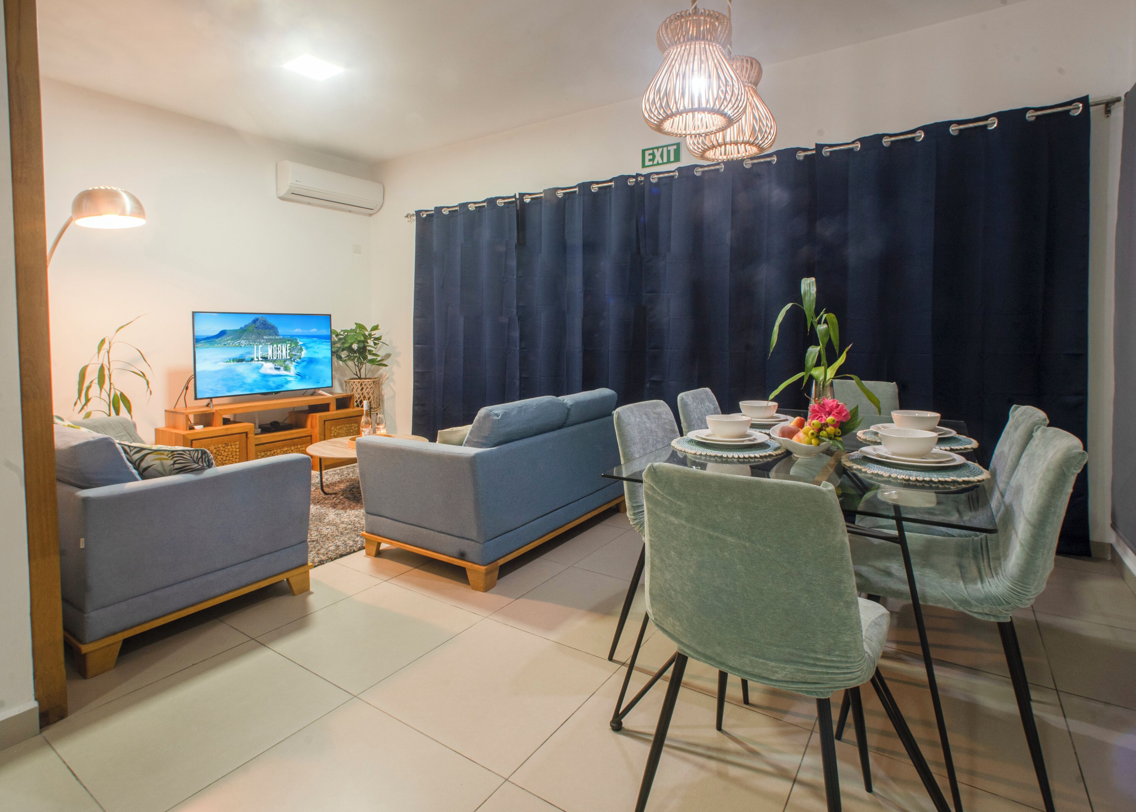 Un salon comprenant un canapé, un téléviseur, une table à manger avec des chaises et un rideau.