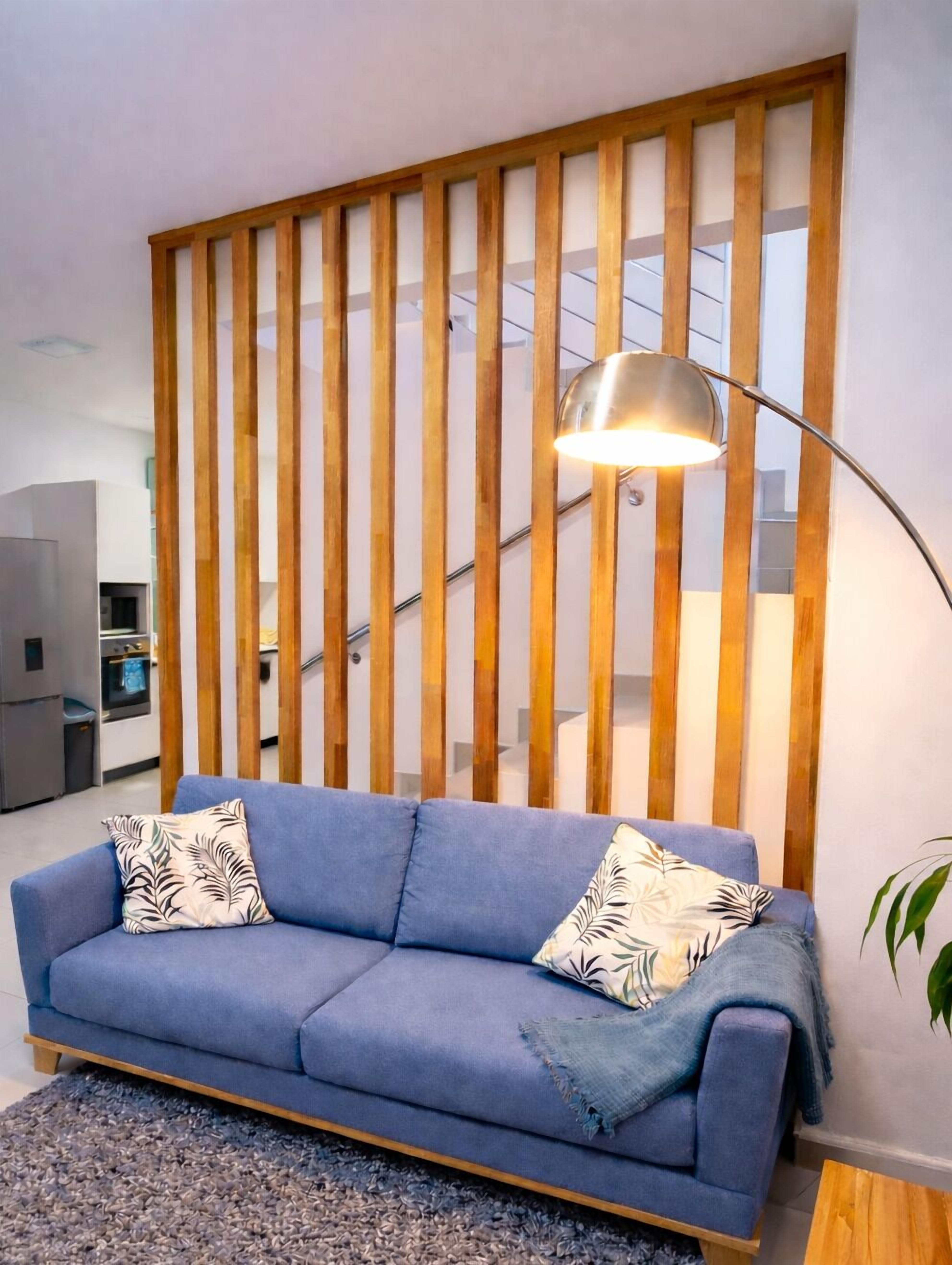 A living room with a blue sofa, wooden slat partition, and a floor lamp.