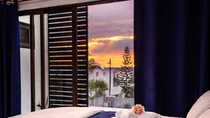 Una camera d'albergo con un letto, vista sul tramonto e una finestra con persiane.
