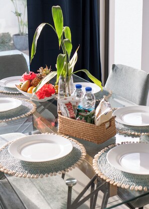 A dining table with placemats, a fruit bowl, a vase with green leaves, and a basket of snacks. - Ocean Blue Villa with private pool at Flic-en-Flac (Flic en Flac)