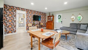 Ein Wohnzimmer mit einer Couch, einem Esstisch mit Stühlen, einem an der Wand befestigten Fernseher und einer Wandtapete mit Muster.