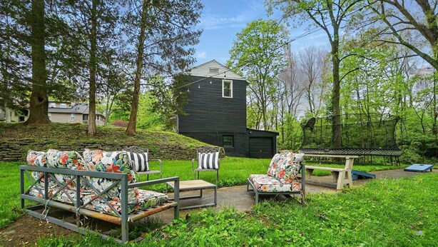 Ein Garten mit einem schwarzen Haus, einer Holzbank und einem blumigen Sofa.