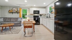 Eine moderne Küche mit weißen Schränken, einem schwarzen Kühlschrank und einem Essbereich mit Holztisch und Stuhl.