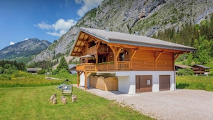 A chalet with a balcony, a gravel driveway, and a mountainous backdrop.