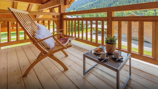 A wooden deck with a wooden chair and a small table with a plant, cookies, and mugs.