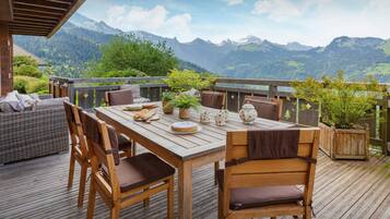 A wooden deck with a table set for dining, surrounded by chairs, overlooking a mountainous landscape.