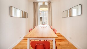 Un espace repas moderne avec une longue table en bois, des chaises rouges et deux grands miroirs accrochés aux murs.
