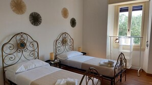A room with two beds, each with a metal headboard and white bedding. There are decorative wall pieces above the beds and a window with blinds to the right. - Beautiful penthouse with loggia and air conditioning, 100 meters from the sea. (Viareggio)