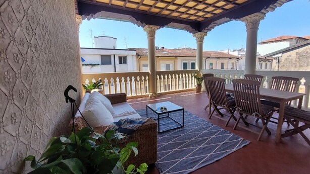 A covered outdoor seating area with a sofa, table, and chairs, overlooking a cityscape. - Beautiful penthouse with loggia and air conditioning, 100 meters from the sea. (Viareggio)