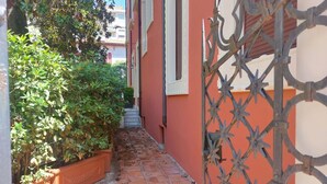 A narrow alleyway with a brick pathway, a metal gate, and a building with a red facade. - Beautiful penthouse with loggia and air conditioning, 100 meters from the sea. (Viareggio)