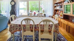 Un coin repas avec une table ronde recouverte d’une nappe à motifs floraux, entourée de chaises blanches. On y trouve également un buffet en bois sur lequel sont disposés des objets décoratifs.