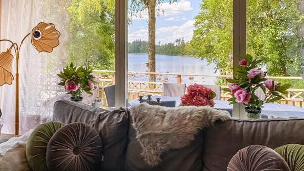 Un coin salon confortable avec un canapé, des coussins et une vue sur un lac, grâce à de grandes fenêtres.