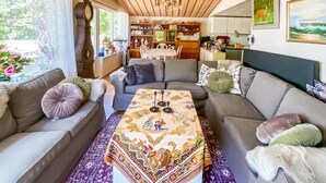 Un salon chaleureux avec un canapé, une table basse recouverte d’une nappe à motifs et une bibliothèque remplie de livres et d’objets décoratifs.