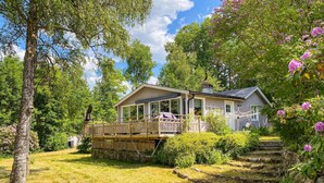 Une cabane en bois dotée d’une terrasse, entourée d’une végétation luxuriante et de plantes en fleurs.