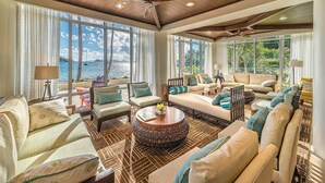Un vaste salon doté d’une grande fenêtre donnant sur la mer, aménagé avec des canapés, une table basse et un ventilateur de plafond.