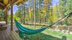 Un hamac sous une terrasse en bois, dans une zone boisée avec des arbres et un ciel dégagé.