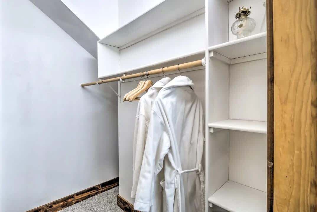 A walk-in closet with white shelves and a wooden rack holding white robes.