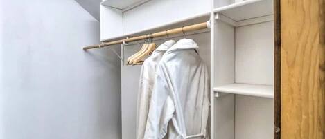 A walk-in closet with white shelves and a wooden rack holding white robes.