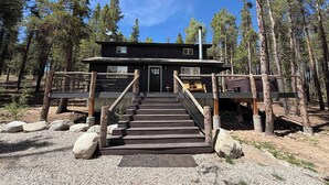 Eine Holzhütte mit einer Holztreppe, die zu einer Terrasse führt, umgeben von Bäumen.