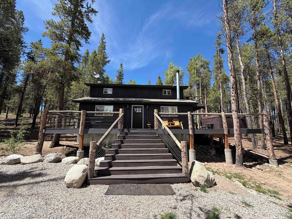 A cabin with a wooden staircase leading to a deck, surrounded by trees.