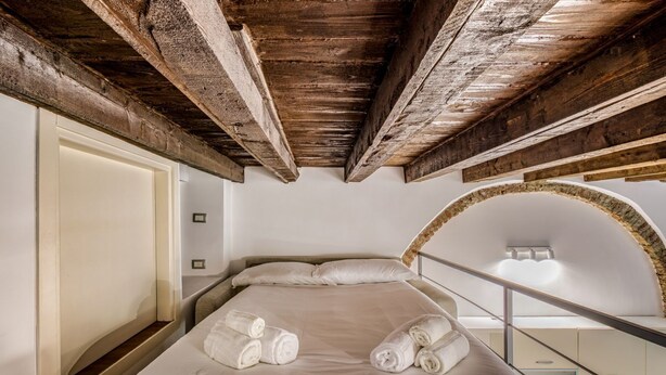 A bedroom with a wooden ceiling, a bed with white linens, and a glass railing. - Ferrari Apartment Colonne (Milano)