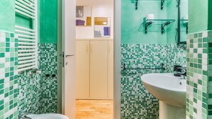 A bathroom with a shower, a sink, and a toilet. There are shelves with toiletries and a towel rack. - Ferrari Apartment Colonne (Milano)