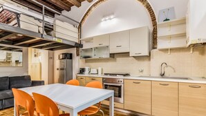 A compact kitchen with modern appliances, a dining area with orange chairs, and a lofted sleeping area with a sofa. - Ferrari Apartment Colonne (Milano)