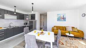 Eine moderne Küche mit grauen Schränken, einem weißen Esstisch mit vier Stühlen und einem gelben Sofa im Wohnbereich.