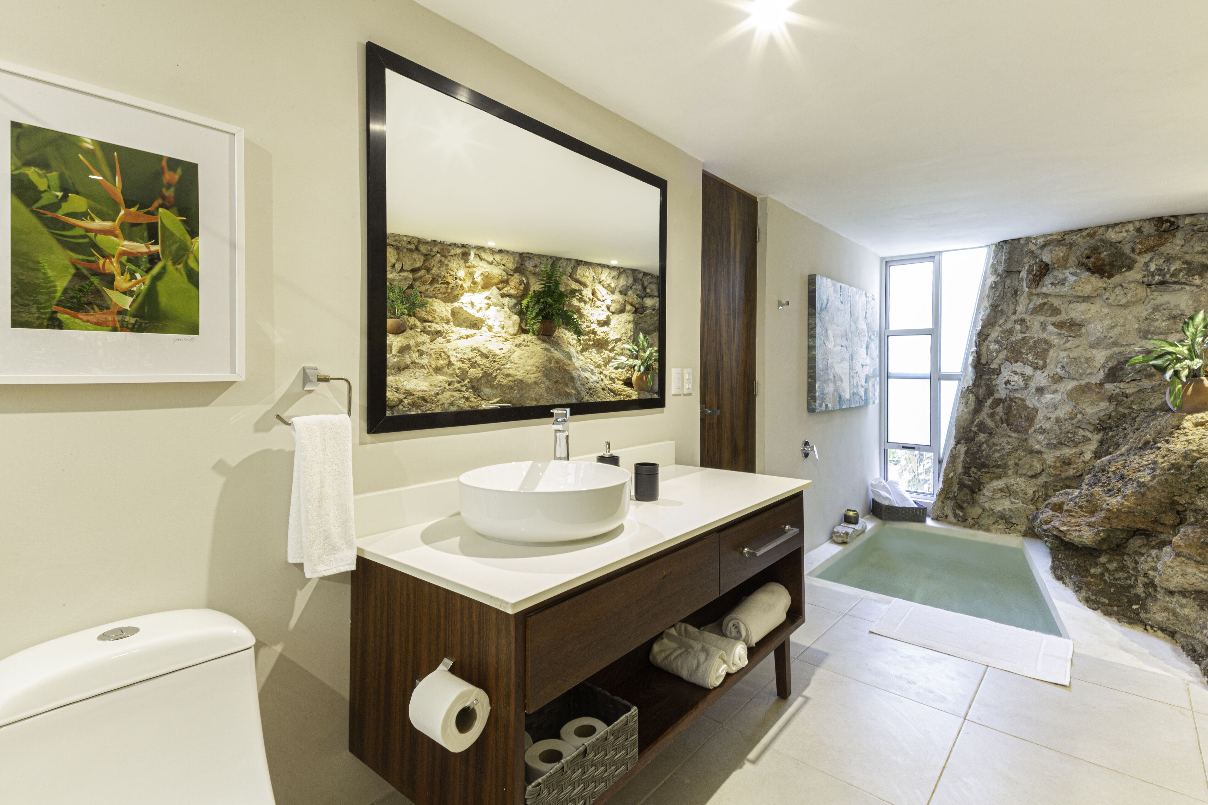 Une salle de bain avec un mur en pierre, un grand miroir, un lavabo et une baignoire.