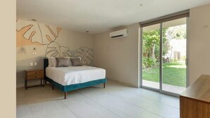 Quarto com cama, mesa de cabeceira, uma obra de arte na parede e porta de vidro deslizando para um jardim.