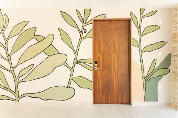 Una habitación con una puerta de madera, una pared con un mural de plantas y una pared estampada a la derecha.