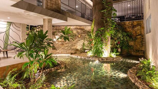 Um jardim interno moderno com fonte, paredes de pedra e diversas plantas.