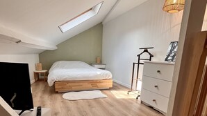 Ein Schlafzimmer mit schrägem Dach, einem Bett, einem Schminktisch, einem Schreibtisch mit Stuhl und einer Hängeleuchte.