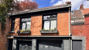 Ein zweistöckiges Gebäude mit Backsteinfassade, schwarzen Fensterrahmen und einer Garage mit schwarzer Tür.