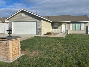 A residential house with a garage, a stone accent wall, a front yard with a lamp post, and a clear sky.
