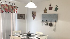 En matplats med ett runt bord, vita stolar, en hängande lampa och dekorationer på väggarna, inklusive en välkomstskylt och föremål med kaffetema.