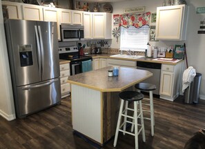 A kitchen with white cabinets, a stainless steel refrigerator, a microwave, a sink, and a wooden island with stools.