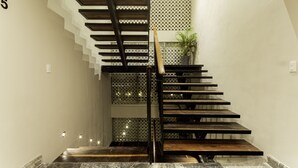 Un escalier moderne avec des finitions en bois et une rampe en métal, menant à un palier agrémenté d’une plante en pot.