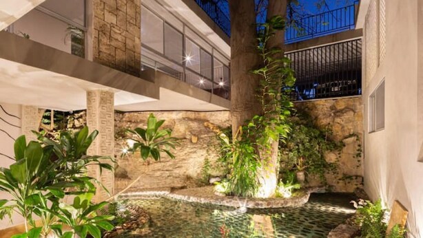 Un bâtiment moderne avec une façade en pierre, un jardin sur le toit et un petit élément décoratif aquatique.
