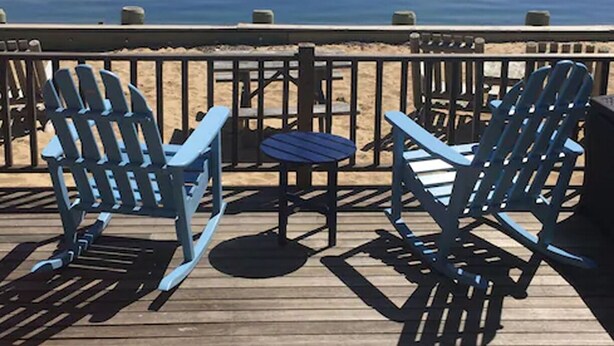 Una terrazza con due poltrone Adirondack e un tavolino, con vista su un mare calmo.