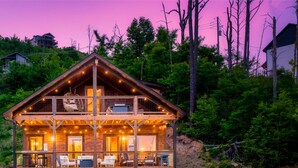 Une cabane en bois à deux étages, dotée d’un balcon et entourée d’une forêt dense.