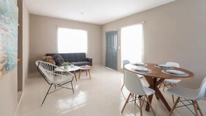 A modern living room with a sofa, a dining table set for four, and a white chair with a metal frame. - Meridia  2 (Yucatan Merida)