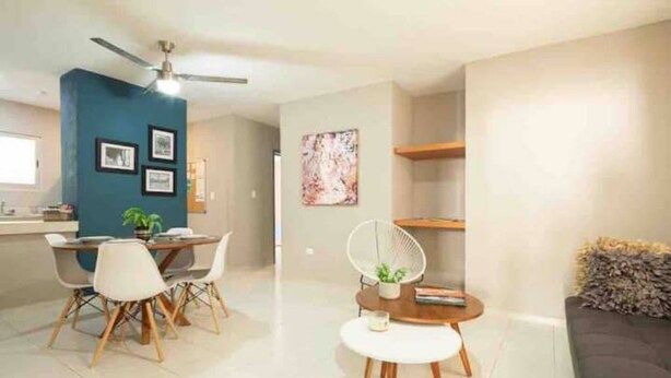 A modern living room with a dark blue accent wall, a dining area with a round table and chairs, a small round coffee table, and a ceiling fan. - Meridia  2 (Yucatan Merida)