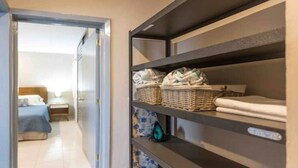 A hotel room with a bed, a nightstand, and a wardrobe with shelves containing folded towels and baskets. - Meridia  2 (Yucatan Merida)