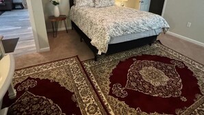 Ein Schlafzimmer mit Bett, Deckenventilator, Nachttisch, Lampe und zwei Teppichen.