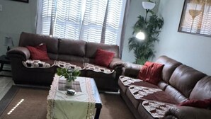 Ein Wohnzimmer mit einem braunen Ledersofa, einem kleinen Tisch mit Spitzentuch und einem großen Fenster mit Vorhängen.