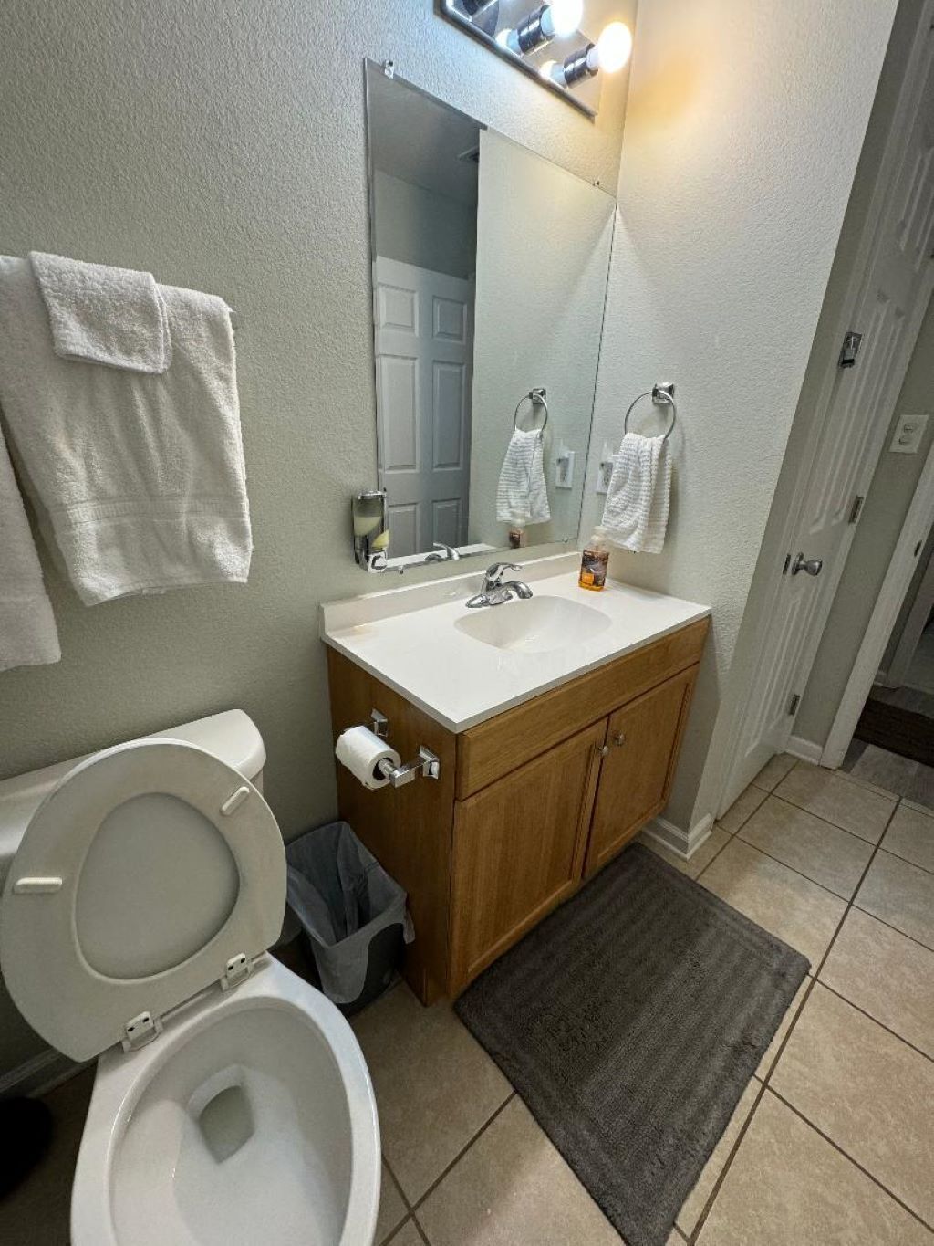 A bathroom with a toilet, sink, mirror, and a trash bin.