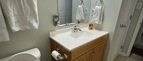 A bathroom with a toilet, sink, mirror, and a trash bin.