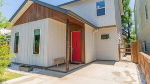 Una casa de dos pisos con puerta roja, un porche pequeño y cerca de madera.