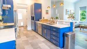 Una cocina moderna con armarios azules, una isla central, electrodomésticos de acero inoxidable e iluminación colgante.